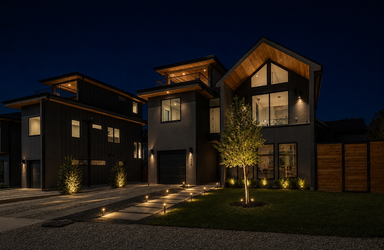 Modern dark home at dusk illuminated with warm low-voltage landscape lighting along the walkway and trees